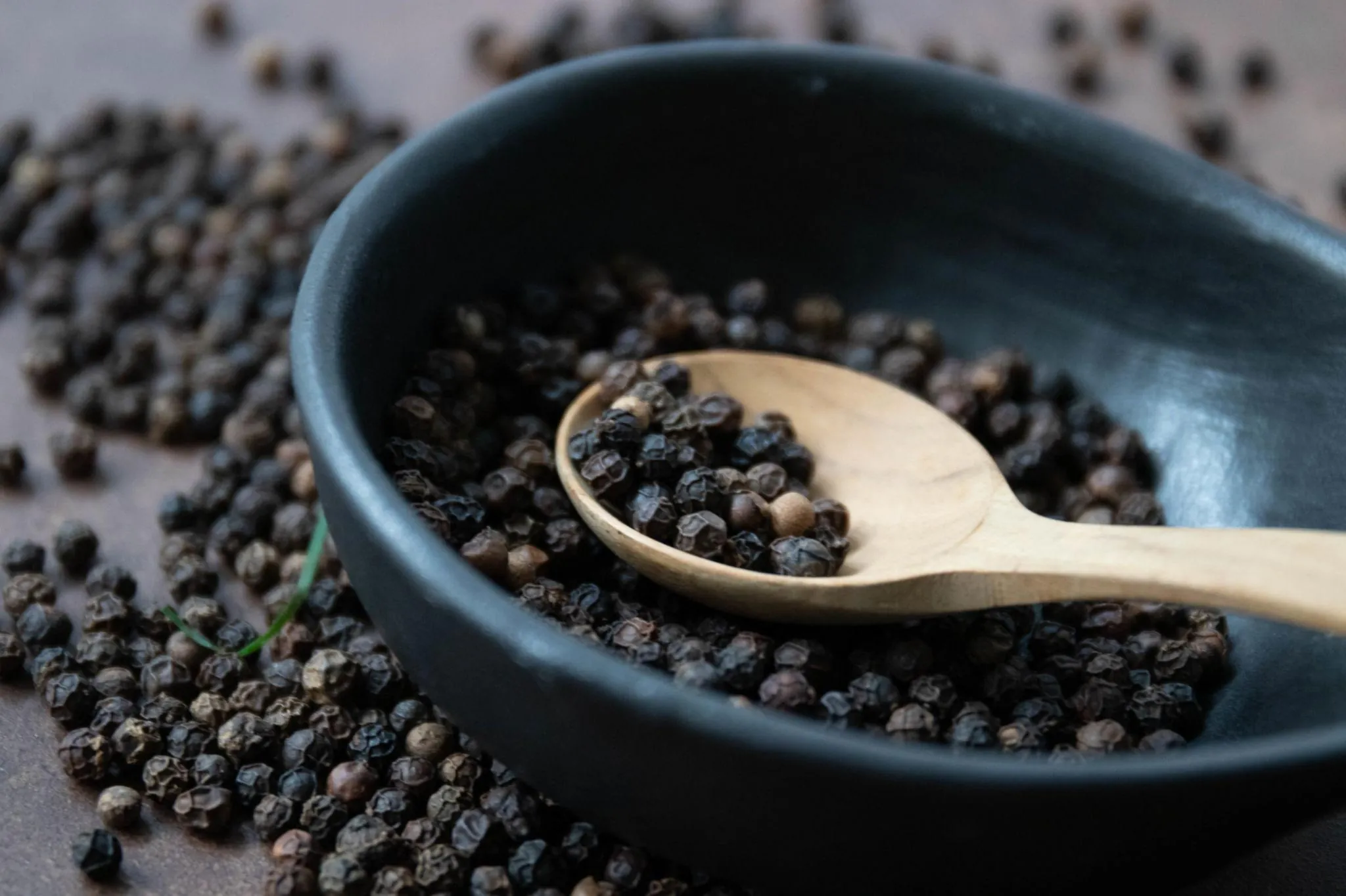 Whole black peppercorns on a textured surface